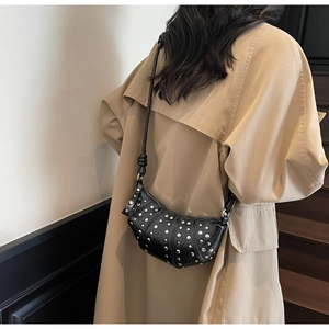 Detail of a black leather hobo bag with silver studs worn with a beige trench coat