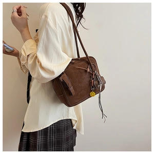 Detailed close-up of brown suede tote bag with decorative buckle and smiley face pendant