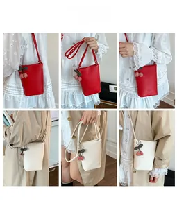 Multiple views of bucket cross-body bags with cherry charms and leather grain texture