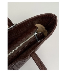 Top-down view of woven dark brown leather tote showing zip closure and beige lining