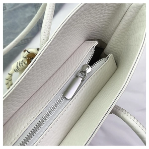 Close-up of smooth metal zipper and pebbled white leather texture on a tote bag