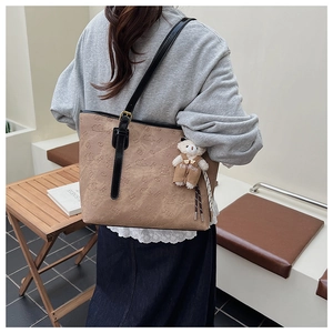 Detailed view of brown embossed tote bag with plush bear charm and black straps