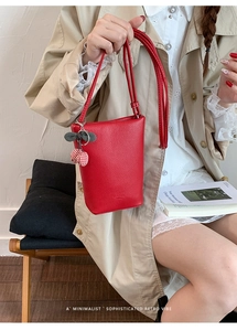 Detail of red pebbled leather bag with cute cherry charm and long slim shoulder strap