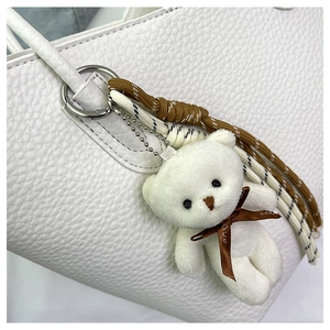 Detail view of a white plush bear charm with a Love bow on a white leather bucket bag