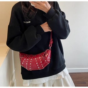 Detail of red crescent shoulder bag featuring silver rivets and knotted strap detail
