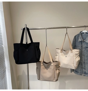 Three minimalist canvas tote bags in black, khaki, and cream with front button pockets