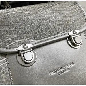 Detail of glitter wave texture and metallic push-lock hardware on silver leather handbag