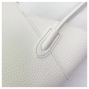 Macro detail of white lychee grain leather texture and fine stitching on shoulder bag