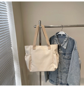Detailed view of beige canvas tote bag side pockets with cinched texture and wide straps