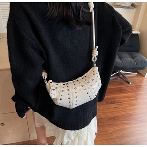 Close-up of white croissant bag with silver rivets and knotted shoulder strap