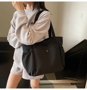 Detail of black canvas tote bag showing side elastic pocket and front buckle pocket