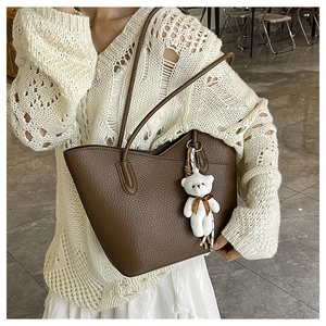 Detail of dark brown leather tote bag with a cute plush bear charm on a model