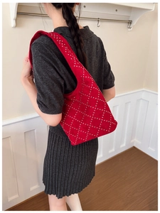Close-up of a red suede shoulder bag featuring silver rivets in a diamond pattern