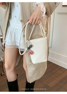 Close-up of white lychee pattern bucket bag with cherry charm and brand logo