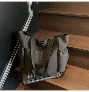 Detail of black canvas tote bag with metal buckle pocket and side drawstring pockets