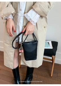 Detail of black litchi texture bucket bag with a cute cherry charm on long strap