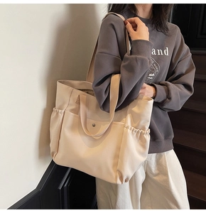 Detail of a large beige canvas tote bag with front snap pocket and side pleat pockets