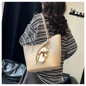 Detail of beige lychee pattern tote bag on model's shoulder with cute teddy bear charm