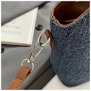 Macro detail of dark blue denim bag with brown leather trim and silver metal hardware