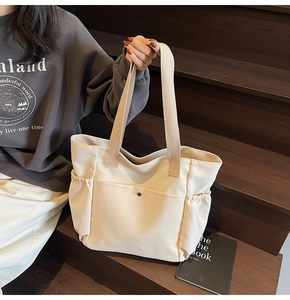 Detailed side view of off-white canvas tote bag featuring elastic side pockets and metal buckle