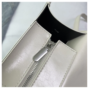 Close-up of a silver rectangular metal zipper on a white synthetic leather denim bag