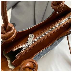 Detail of metal zipper closure and brown faux leather lining on denim bucket bag