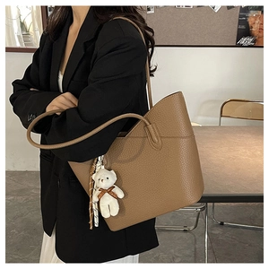 Detail of brown leather tote bag with small bear charm accessory on model's shoulder