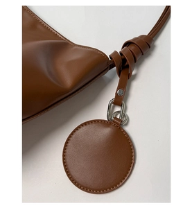 Detail der braunen Leder-Beuteltasche mit Knotengurt und kreisförmigem Anhänger-Zubehör