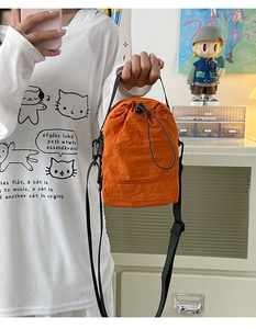Close-up of orange drawstring bucket bag with black wide strap and nylon texture detail