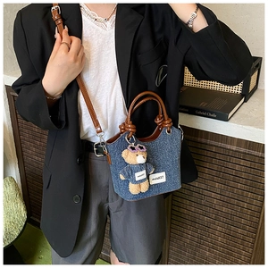 Detail of denim bucket bag with plush bear charm and adjustable leather shoulder strap