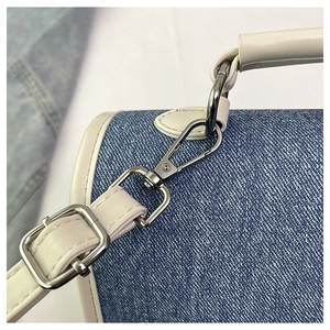 Close-up of denim backpack with leather trim, white stitching, and silver metal hardware