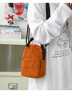 Detail view of orange nylon crossbody bucket bag with drawstring and fashion label