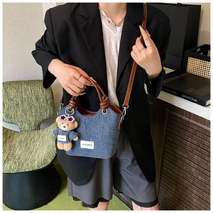 Detail of denim bucket bag with brown leather handle and cute teddy bear charm