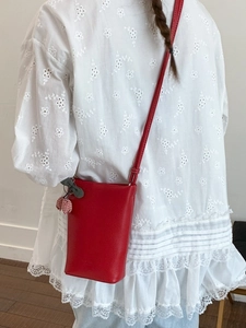 Fashionable red leather tote bucket bag with cherry charm shown on model's back