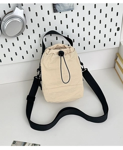 Detail of beige drawstring bucket bag with black adjustable strap on pegboard background