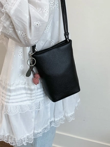 Chic black lychee leather tote bucket bag with cherry charm accessory on white dress
