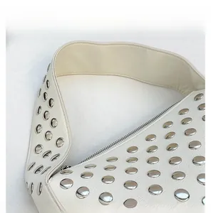 Detail of white leather shoulder bag with silver rivet studs and a wide comfort strap