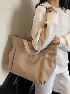 Large khaki canvas tote bag with side pockets and metal clasp shown on a model's shoulder
