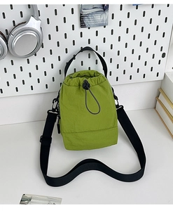 Detail of green nylon drawstring bucket bag with adjustable strap in casual setting