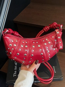 Red leather moon bag with silver studs and woven strap in a stylish handheld pose