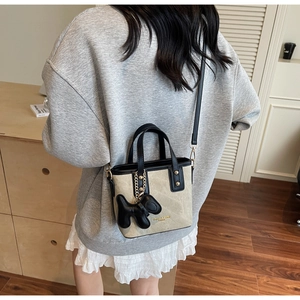 Détail du sac seau en toile avec bordure en cuir noir et breloque chiot sur un mannequin