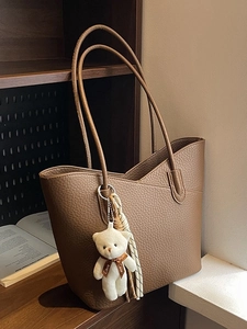 Brown leather tote bag with teddy bear pendant on a wooden shelf in natural light