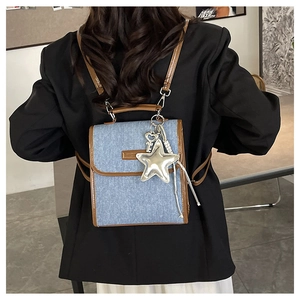 Detail of denim backpack with brown leather trim and silver star pendant on model