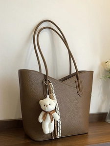 Brown lychee leather tote bag with plush bear charm and striped scarf in home setting