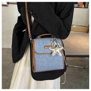 Detail of blue denim square bag with silver star pendant and brown leather trim accents