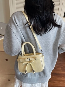 Petit sac à main jaune crème avec nœud décoratif et texture plissée porté par un modèle
