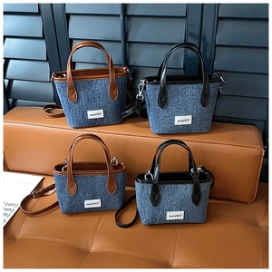 Detail view of denim bucket bag set with contrast leather trim and branding label