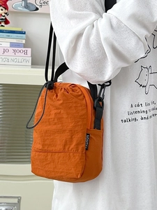 Orange crossbody phone bag with drawstring closure and fashion label on shoulder strap