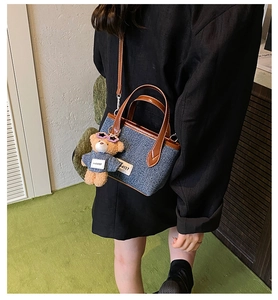 Detail of denim bucket bag with brown leather handles and a cute plush bear charm