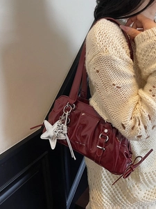 Deep wine red glossy shoulder bag with pleats and star charm worn on white knit sweater